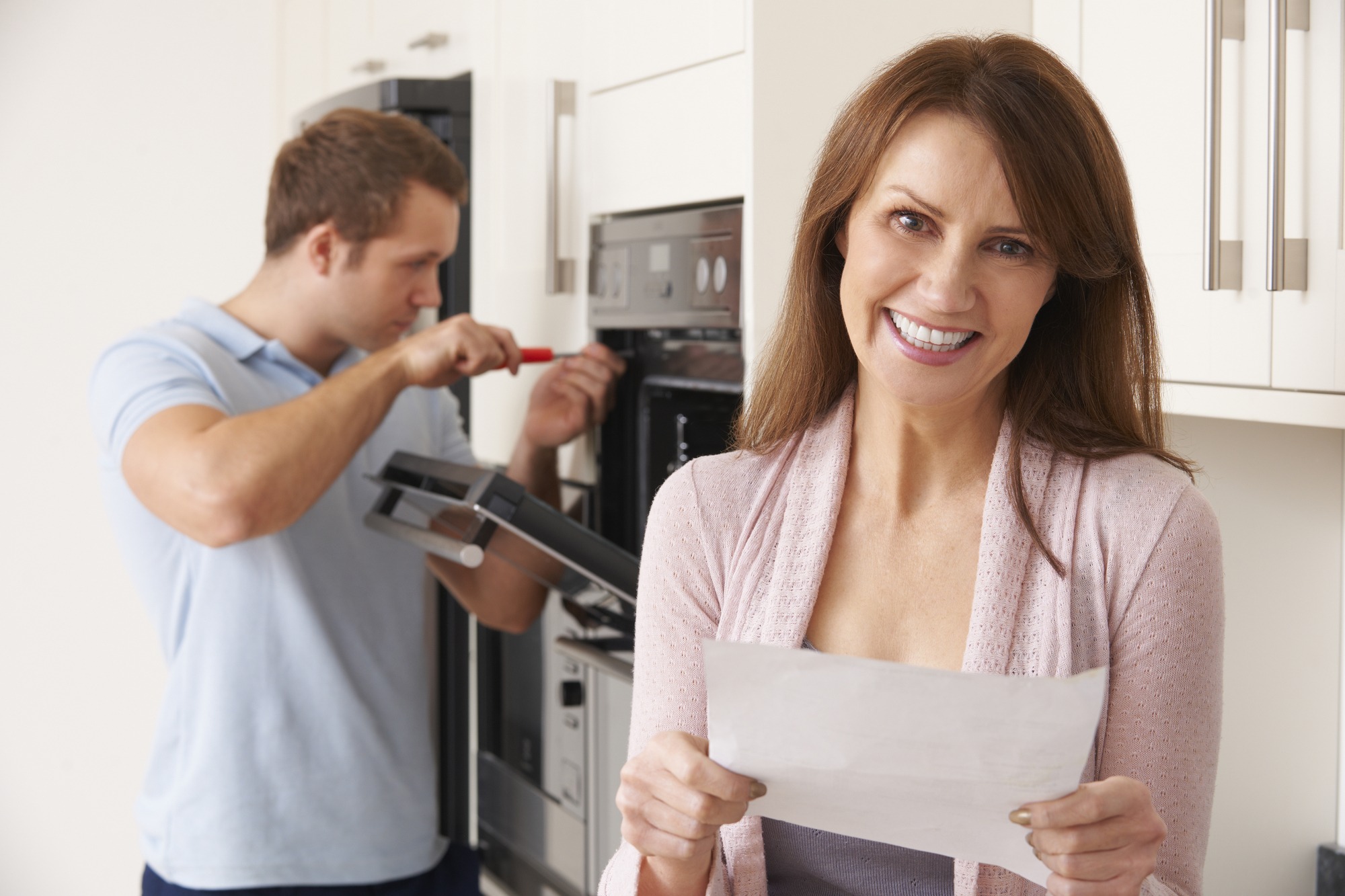 A woman stands beside a man who is fixing the oven